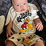 baby, blue_eyes, cartoon, child, clothing, cute, expression, fabric, foot, hand, indoor, infant, mickey_mouse, person, pluto, portrait, shorts, sitting, stroller, tshirt