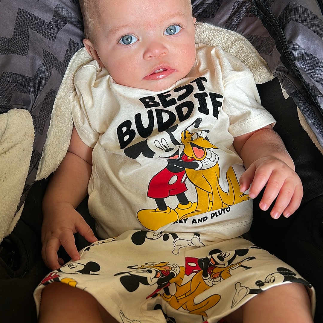 Rhayne joined the competition — help win amazing prizes! baby, blue_eyes, cartoon, child, clothing, cute, expression, fabric, foot, hand, indoor, infant, mickey_mouse, person, pluto, portrait, shorts, sitting, stroller, tshirt