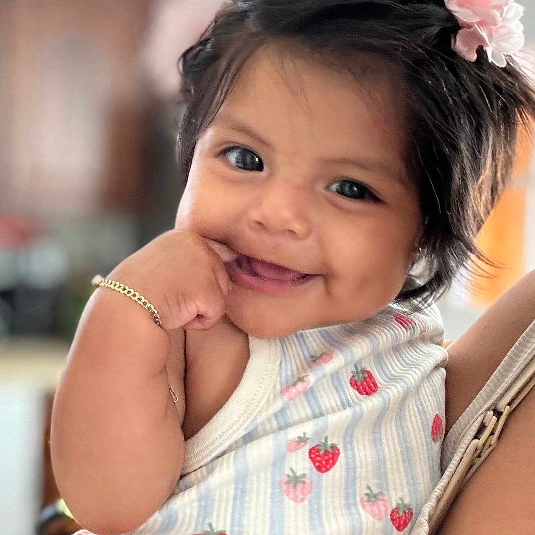 Karelyn joined the competition — help win amazing prizes! baby, child, smiling, cute, girl, flower, hair_accessory, bracelet, strawberry_pattern, pink_skirt, hand, portrait, happy, person, indoor, closeup, infant, playful, dimple, holding