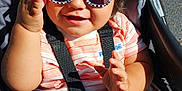 Dominic is registered to the contest to win money with this photo: toddler, child, sunglasses, stroller, smiling, sunlight, happy, baby, seatbelt, casual_clothing, striped_shirt, outdoor, person, young_child, cute, fashion, hands, portrait, playful, shiny_hair