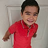 child, smiling, portrait, indoors, red_shirt, polo_shirt, short_hair, happy, face, teeth, standing, door, white_background, home, close_up, playful, young, person, photography, grinning
