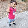 Dominic is registered to the contest to win money with this photo: child, boy, toddler, smiling, portrait, outdoor, standing, posing, pointing, pink_shirt, checkered_shorts, sneakers, short_hair, face, person, sidewalk, concrete, leaves, plants, background