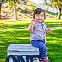 child, toddler, outdoor, grass, bench, crate, shirt, pants, sneakers, smile, birthday, celebration, number_one, sunlight, tree, park, greenery, happy, portrait, casual_clothing