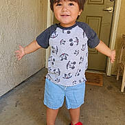 Dominic is registered to the contest to win money with this photo: child, toddler, portrait, smiling, standing, outdoors, doorway, door, garage, concrete, wall, mickey_mouse, t_shirt, shorts, sandals, red_shoes, arms_outstretched, brown_hair, home_entrance, daylight