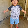 child, toddler, portrait, smiling, standing, outdoors, doorway, door, garage, concrete, wall, mickey_mouse, t_shirt, shorts, sandals, red_shoes, arms_outstretched, brown_hair, home_entrance, daylight