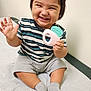 toddler, child, smiling, happy, teething_toy, striped_shirt, shorts, socks, sitting, indoor, medical_table, baby, cute, hand, face, expression, playful, young_child, person, casual_clothing