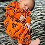 newborn, baby, sleeping, orange_clothing, pumpkin_pattern, onesie, infant, blanket, camo_pattern, feet, hands, cute, cozy, resting, child, portrait, indoors, soft_texture, peaceful, young