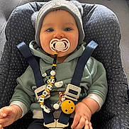Eden a rejoint le concours — aidez-le/la à gagner de superbes lots ! baby, pacifier, beanie, car_seat, child, blue_eyes, clothing, cute, face, hand, indoor, infant, jacket, person, seatbelt, smile, toy, young_child, warm_clothing, happy