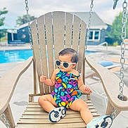 Myraa is registered to the contest to win money with this photo: toddler, child, sunglasses, swing, wooden_chair, poolside, colorful_clothing, romper, summer, outdoor, relaxing, footwear, concrete, daylight, vacation, casual, baby, fun, cute, leisure