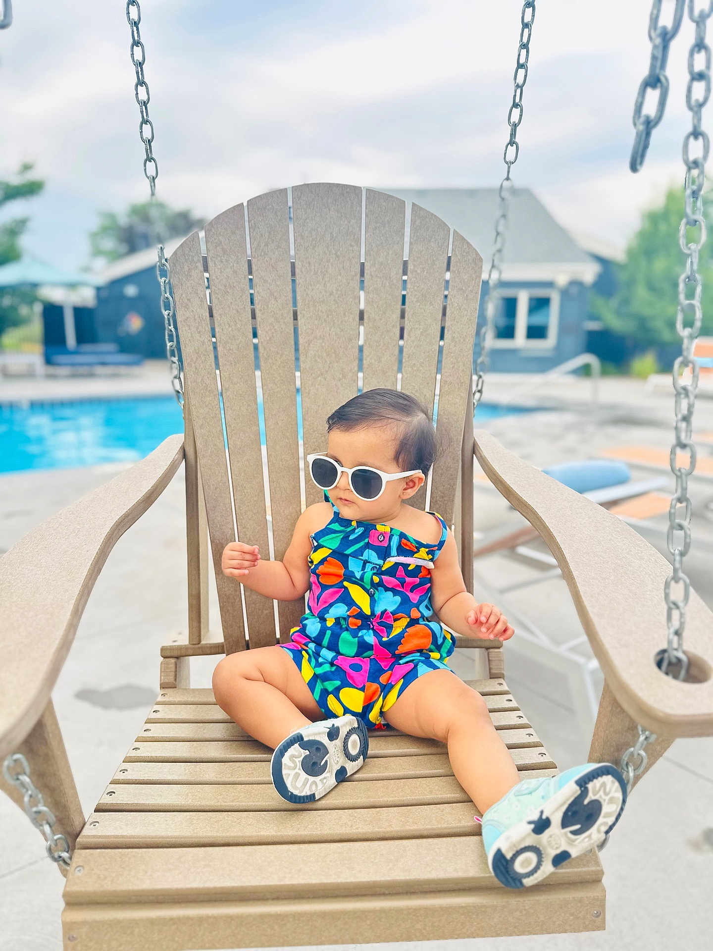 Myraa is registered to the contest to win money with this photo: toddler, child, sunglasses, swing, wooden_chair, poolside, colorful_clothing, romper, summer, outdoor, relaxing, footwear, concrete, daylight, vacation, casual, baby, fun, cute, leisure