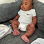 baby, infant, onesie, nike_logo, couch, gray_couch, baby_wipes, plastic_bag, indoors, child, sitting, chubby, cute, relaxed, portrait, skin, furniture, home, young_child, person