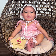 Rayanah joined the competition — help win amazing prizes! baby, child, infant, smiling, pink_clothing, bonnet, rattan_chair, woven_chair, cushion, wooden_floor, milestone_sign, 5_months, flower_sign, cute, sitting, indoors, portrait, happy, person, young_child
