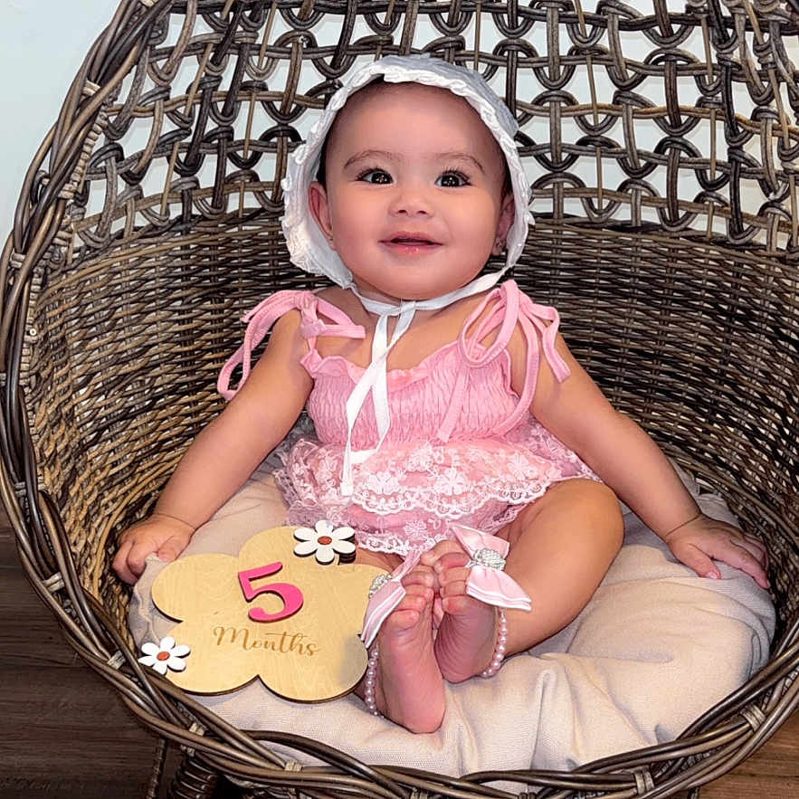 Rayanah joined the competition — help win amazing prizes! baby, child, infant, smiling, pink_clothing, bonnet, rattan_chair, woven_chair, cushion, wooden_floor, milestone_sign, 5_months, flower_sign, cute, sitting, indoors, portrait, happy, person, young_child