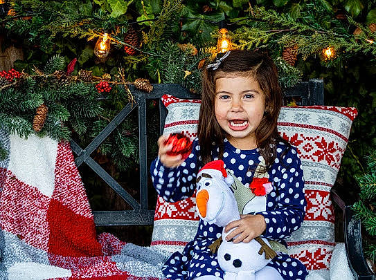 Isabel is registered to the contest to win money with this photo: baby_toddler_clothing, christmas, christmas_decoration, christmas_eve, christmas_ornament, christmas_tree, conifer, event, fictional_character, holiday, holiday_ornament, interior_design, ornament, pattern, person, pine_family, pleased, stuffed_toy, textile, toy