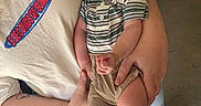 Lucas joined the competition — help win amazing prizes! baby, smile, happy, person, child, striped_shirt, shorts, adult, holding, tattoo, tshirt, graphic, floor, concrete, footwear, casual_clothing, indoor, portrait, closeup, human