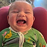 baby, laughing, smiling, green_onesie, animal_print, infant, child, happy, portrait, indoor, baby_swing, carpet, floor, couch, soft_lighting, comfortable, cute, joyful, closeup, person