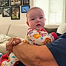 Lucas is registered to the contest to win money with this photo: baby, infant, child, pajamas, basketball, person, arm, hand, couch, sofa, living_room, window, curtains, picture_frame, wall_art, animal_photos, indoor, comfort, holding, relaxation