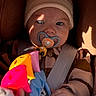 Waylen a rejoint le concours — aidez-le/la à gagner de superbes lots ! baby, beanie, blue_eyes, car_seat, close_up, colorful_toy, cozy, face, hands, hat, infant, pacifier, plush, portrait, seatbelt, shadow, smiling, striped_clothing, sunlight, toy