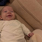 Waylen a rejoint le concours — aidez-le/la à gagner de superbes lots ! baby, infant, smile, face, onesie, blanket, couch, lying_down, hand, cheek, portrait, cozy, fabric, skin, happy, bedroom, soft_texture, knee, home_interior, close_up