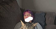 Ella joined the competition — help win amazing prizes! person, cat, couch, blanket, indoor, relaxing, purple_hair, tabby_cat, pet, feline, resting, cozy, home, casual, comfort, seated, furniture, wall, soft_lighting, domestic