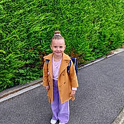 élise participe au concours pour gagner de l'argent avec cette photo : backpack, casual_clothing, child, coat, fashion, girl, greenery, hair_bun, happy, hedge, jacket, nature, outdoor, portrait, purple_pants, sidewalk, smile, standing, urban, white_shoes