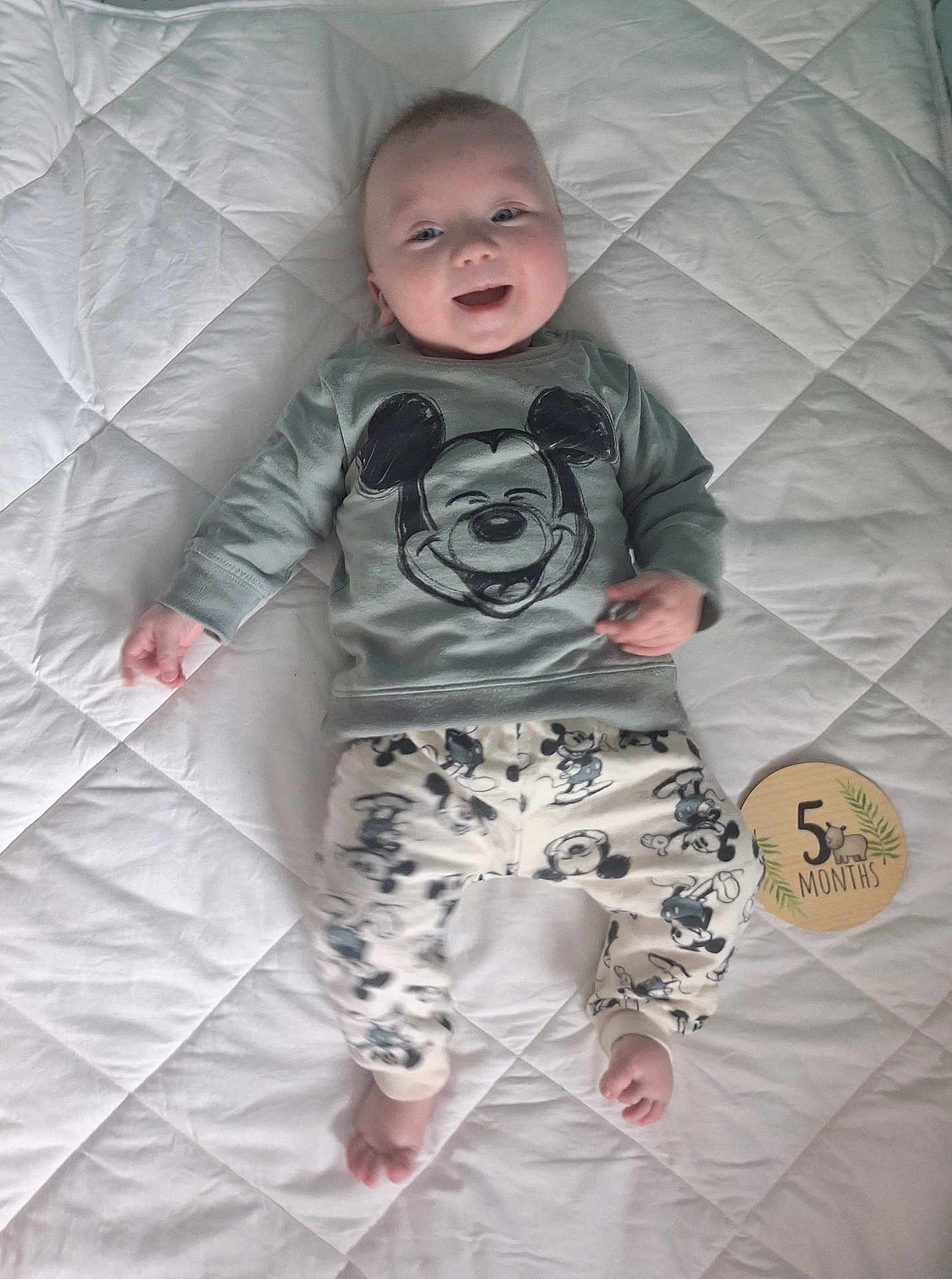 Malo participe au concours pour gagner de l'argent avec cette photo : baby, infant, smiling, lying_down, mickey_mouse, clothing, pants, sweatshirt, blanket, quilted, milestone, wooden_plaque, 5_months, cute, happy, face, foot, hand, indoors, person