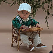 Aziel joined the competition — help win amazing prizes! baby, child, wicker_chair, hat, green_shirt, beige_background, plants, indoor, portrait, curious_expression, small_chair, sitting, brown_shoes, bow_tie, suspenders, cute, studio_photo, infant, decor, young_child