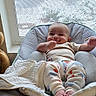 Aziel is registered to the contest to win money with this photo: baby, baby_chair, baby_garment, blanket, clothing, comfort, cushion, face, footwear, happy, home, indoor, infant, natural_light, person, seated, smiling, window, window_screen, winter_outside