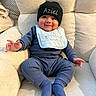 armchair, baby, beanie, bib, blue_clothing, child, comfort, cozy, cute, face, happy, hat, indoor, infant, knitwear, person, plush_furniture, portrait, sitting, smile