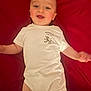 baby, baby_clothing, cheeks, child, cute, eyes, face, happy, head, human, indoor, infant, lying_down, mouth, person, red_background, short_sleeves, skin, smiling, white_onesie