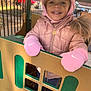 casual, child, cute, daylight, face, fence, happy, hood, mittens, outdoor, park, person, pink_jacket, playground, playtime, smiling, toddler, toy, warm_clothes, winter_clothing