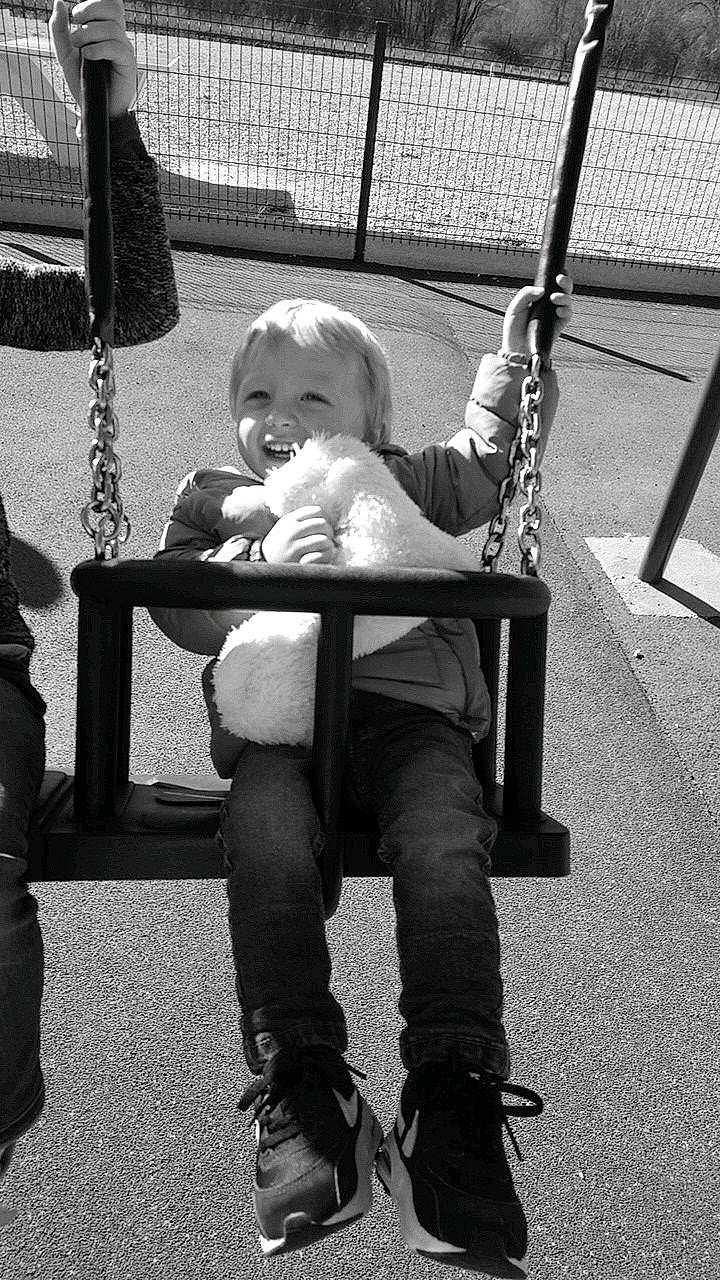 Nino a rejoint le concours — aidez-le/la à gagner de superbes lots ! black_and_white, child, joy, monochrome, outdoor_play_equipment, person, photography, playground, public_space, sitting, smile, snapshot, style, swing, toddler