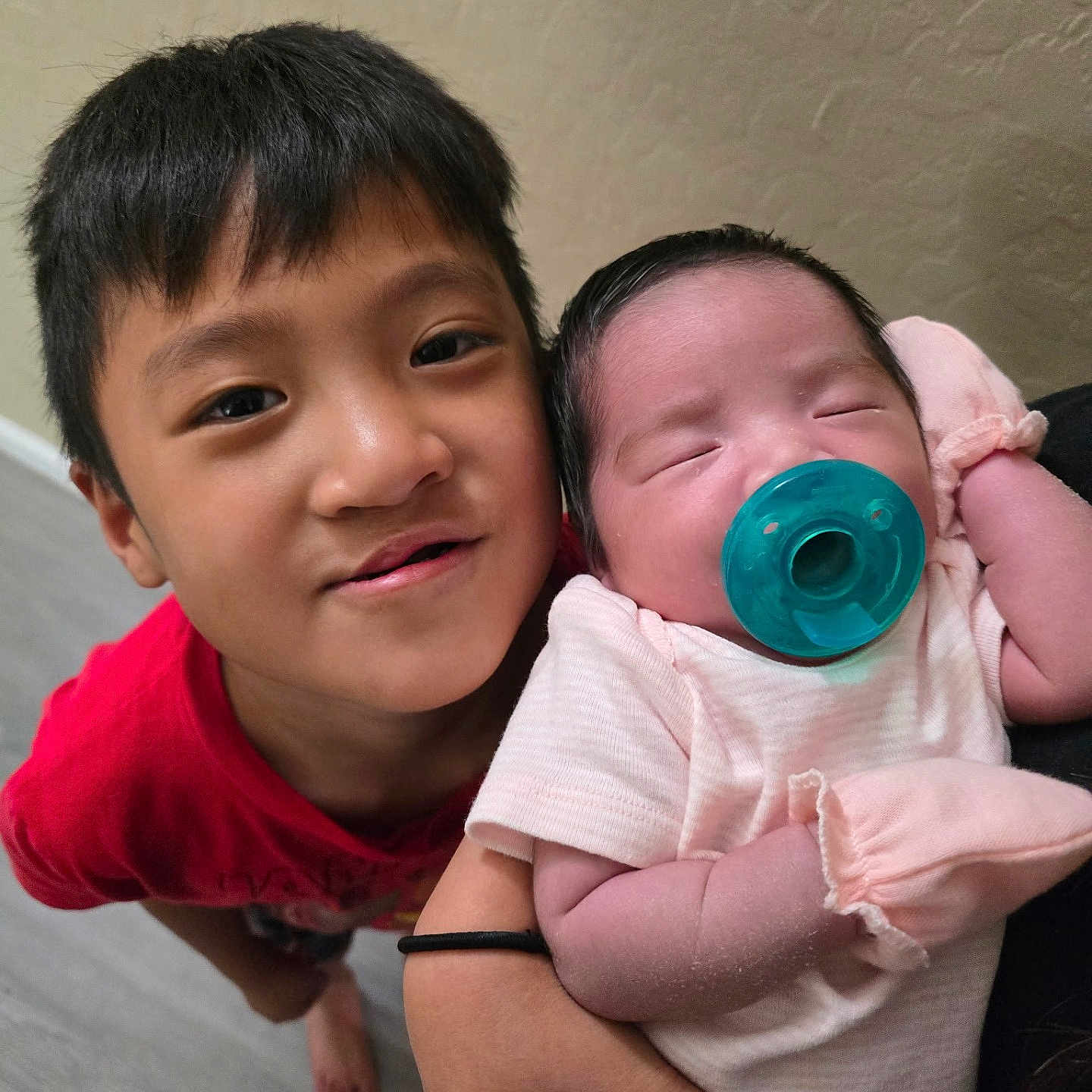 Jayzen is registered to the contest to win money with this photo: arm, baby, child, cute, face, family, hair, hand, happy, holding, indoor, infant, love, newborn, pacifier, person, red_shirt, sibling, skin, sleeping