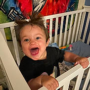 Anna is registered to the contest to win money with this photo: baby, crib, child, happy, smiling, indoor, toddler, furniture, colorful, tapestry, nursery, hair, expression, playful, hand, grip, clothing, person, room, background