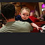 Raiden joined the competition — help win amazing prizes! baby, child, person, shoulder, back, indoor, blurred_background, cross, church, seated, people, serious_expression, holding, dark_hair, blue_clothing, green_shirt, focus, portrait, candid, gathering