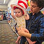 baby, bookshelf, bookstore, carpet, casual_wear, child, clothing, curious, giraffe_print, hat, holding, indoor, keys, kids_fiction, man, person, serious, shopping, striped_hat, young_adult