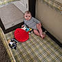 baby, child, playpen, toys, plaid, onesie, floor, carpet, indoor, infant, face, looking, curious, soft_toy, red_toy, mickey_mouse, relaxed, home, small, person