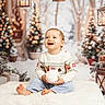 bokeh_lights, child, christmas_tree, cozy, decorations, festive, gift_box, happy, holiday, lantern, ornaments, pinecone, plush_rug, portrait, sitting, smile, snow, sweater, toddler, winter