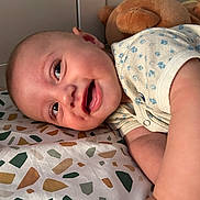 Liham participe au concours pour gagner de l'argent avec cette photo : baby, infant, smiling, face, onesie, bedspread, patterned, plush_toy, teddy_bear, lying_down, happy, child, cute, skin, head, arm, indoors, closeup, portrait, young
