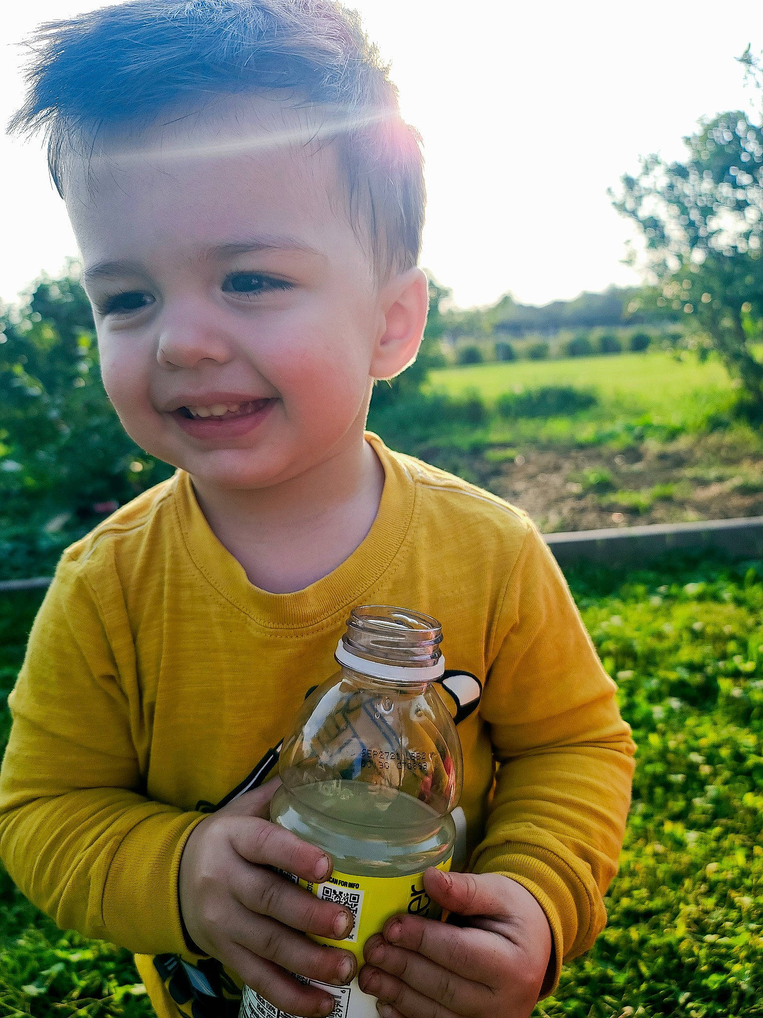 Jaxxon is registered to the contest to win money with this photo: bottle, drink, drinking_water, drinkware, finger, glass_bottle, grass, hand, happy, joy, natural_environment, people_in_nature, person, plant, plastic_bottle, sky, smile, summer, sunlight, tree