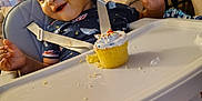 Zayvion is registered to the contest to win money with this photo: celebration, child, clothing, cupcake, curtains, face, food, frosting, furniture, happy, high_chair, home, indoor, messy, playful, seatbelt, smiling, sprinkles, table, toddler