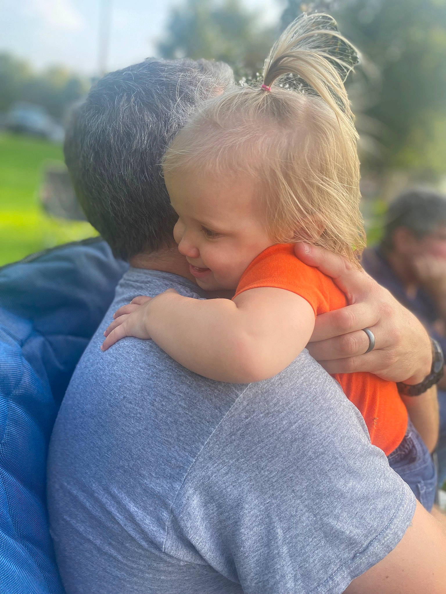 Maggie is registered to the contest to win money with this photo: baby, baby_products, child, electric_blue, event, fun, gesture, grass, happy, hug, leisure, people_in_nature, person, recreation, shoulder, sitting, sky, t_shirt, toddler, tree