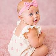 Hazel is registered to the contest to win money with this photo: baby, child, infant, pink_bow, romper, strawberry_pattern, fluffy_rug, pink_background, sitting, cute, portrait, blue_eyes, headband, soft_lighting, adorable, smiling, skin, one_person, indoor, young_child
