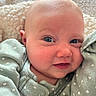 baby, infant, face, blue_eyes, smile, green_clothing, hearts_pattern, blanket, cozy, close_up, cute, newborn, soft_texture, skin, person, portrait, child, warm, resting, happy