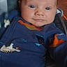 baby, infant, child, portrait, face, wide_eyes, looking_at_camera, car_seat, pacifier, onesie, blue_clothing, colorful_clothing, seated, indoor, close_up, head, hair, smiling, baby_carrier, cozy