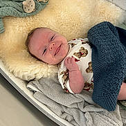 Dylan is registered to the contest to win money with this photo: baby, bed, blanket, clothing, comfort, cozy, cute, face, happy, indoors, infant, knitted_blanket, newborn, pacifier, person, resting, sleeping_area, smiling, soft_texture, towel