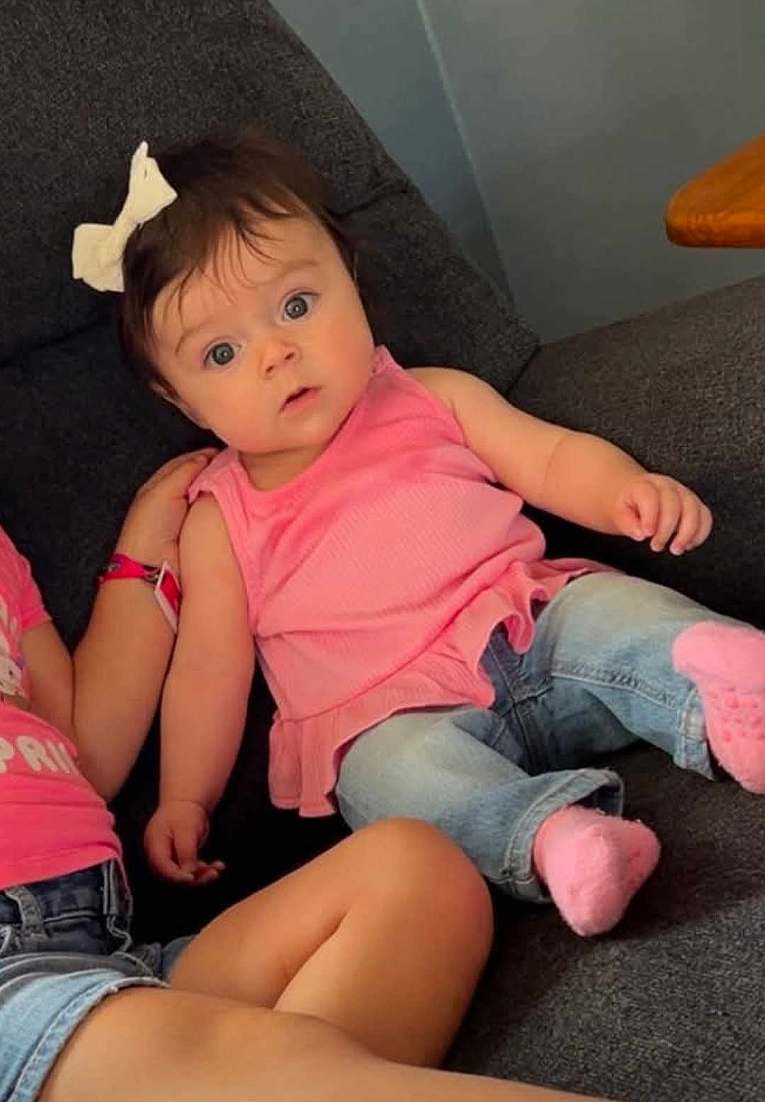 Ariah joined the competition — help win amazing prizes! baby, child, girl, pink_top, jeans, white_bow, couch, indoor, curious, wide_eyes, casual_clothing, sitting, socks, hand, arm, leg, dark_gray, furniture, portrait, family
