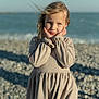 Veronika participe au concours pour gagner de l'argent avec cette photo : child, girl, beach, sea, sky, rocks, dress, blonde_hair, portrait, outdoor, wind, hands_on_face, casual_clothing, sunlight, nature, smile, young, person, daytime, scenery