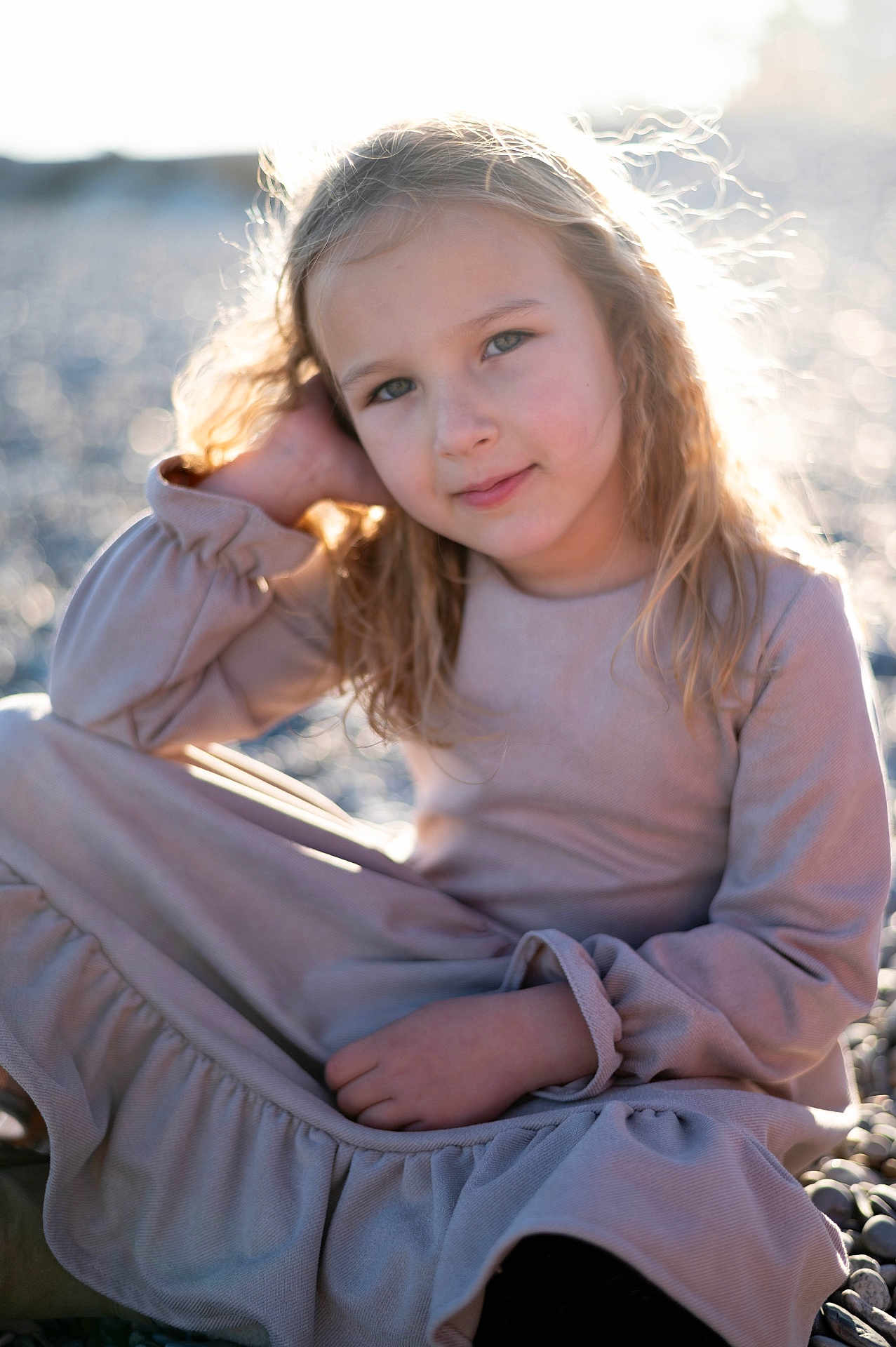 Veronika participe au concours pour gagner de l'argent avec cette photo : child, girl, blonde_hair, long_hair, dress, beach, pebbles, sunlight, backlit, portrait, smile, sitting, casual_pose, outdoor, nature, soft_light, young, happy, relaxed, daytime