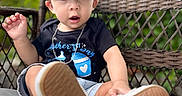 Avery is registered to the contest to win money with this photo: toddler, child, cap, black_shirt, mother's_day, chain_necklace, shorts, sneakers, shoe_sole, wicker_chair, cushion, outdoor, greenery, portrait, curious_expression, casual_clothing, baby, seated, daylight, closeup